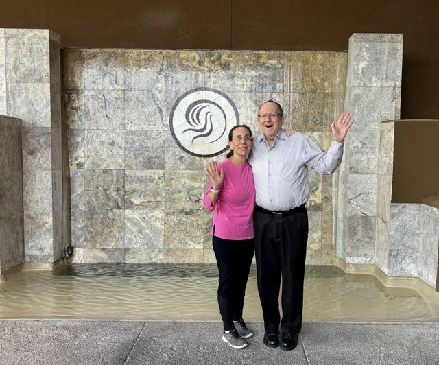 Linda and Naftali Schwartz smiling together in front of a stone fountain