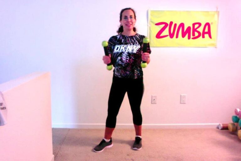 Linda in 2020 holding hand weights in front of a Zumba banner